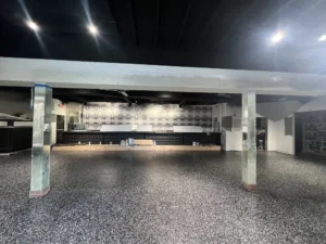 Large commercial space under renovation with speckled floor, bar, and reflective pillars.