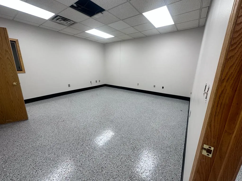 Empty room with white walls, black baseboards, and shiny gray speckled epoxy floor.